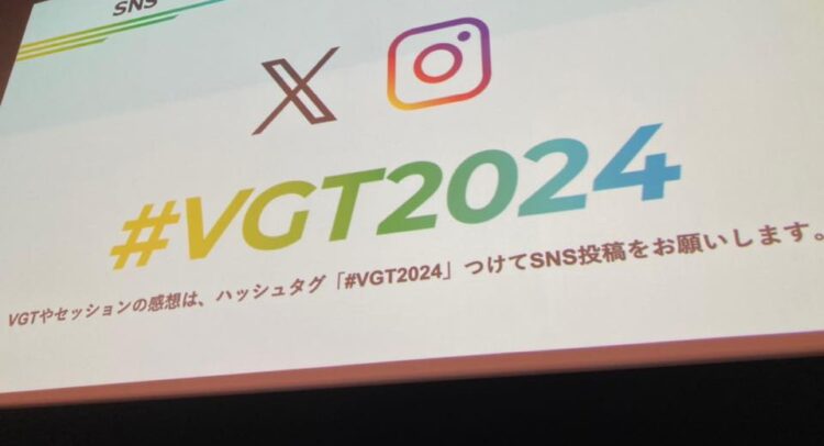 VIDEOGRAPHERS TOKYO 2024のイベント会場で、スクリーンに表示されたスライドの写真。スライドには「SNS x Instagram #VGT2024」と大きく書かれており、「VGTやセッションの感想は、ハッシュタグ『#VGT2024』つけてSNS投稿をお願いします」とのメッセージが表示されている。スライドはイベントのSNSキャンペーンを案内している。スクリーンの下部には椅子と机が見える。