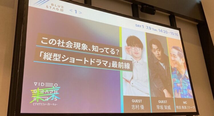 この写真は、「縦型ショートドラマ」に関するイベントやトークセッションの様子を示すスライドのようです。タイトルには「この社会現象、知ってる？『縦型ショートドラマ』最前線」と書かれており、縦型ショートドラマについて議論する場であることがわかります。 左下にイベントのロゴと「VIDEOGRAPHERSTOKYO 2024」という表記があり、ビデオ関係のカンファレンスや展示会の一部かもしれません。ゲストには、志村優さんと早坂架威さん、そしてMCとして熊田勇真（マーク）さんが参加している。