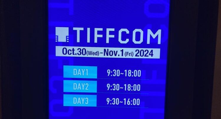 この画像は「TIFFCOM」の開催案内を示すディスプレイです。イベントは2024年10月30日（水）から11月1日（金）までの3日間開催される予定で、それぞれの開催時間も記載されています。 DAY 1：9:30 ～ 18:00 DAY 2：9:30 ～ 18:00 DAY 3：9:30 ～ 16:00 TIFFCOMは、東京国際映画祭（TIFF）に連動して開催される映像やコンテンツのマーケットイベントで、映像業界関係者が集まるビジネスマッチングの場としても知られています。