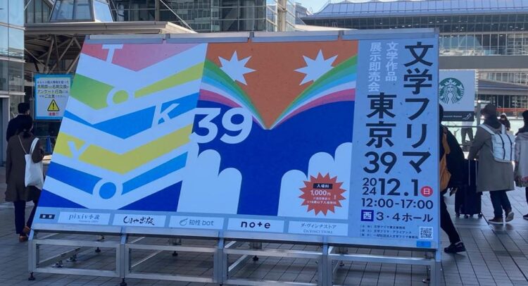 東京ビッグサイト前に設置された『文学フリマ東京39』の大型看板。カラフルなデザインに「TOKYO 39」の文字が描かれ、開催日である2024年12月1日(日)や会場（西3・4ホール）の情報が明記されている。訪れる人々の姿も写り込み、イベントの盛り上がりを感じさせる。