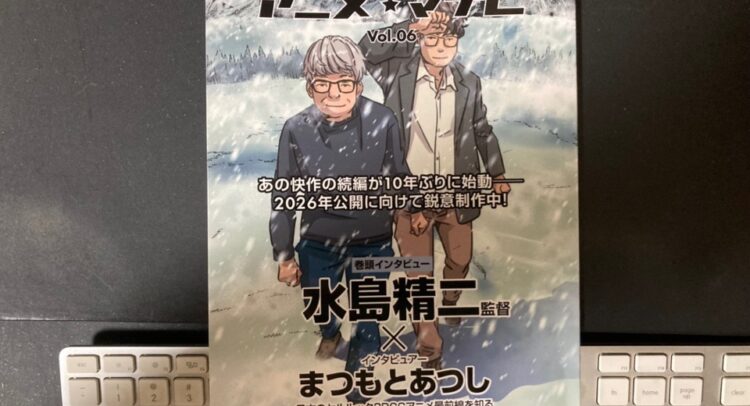 「アニメ・マナビ Vol.06」という冊子の表紙が写っていますね。表紙には、監督の水島精二さんとデジタル制作に詳しいと思われるまつもとあつしさんが登場している様子が描かれています。また、「10年ぶりに始動」「2026年公開に向けて鋭意制作中！」という文言から、注目の続編プロジェクトが紹介されていることがわかります。