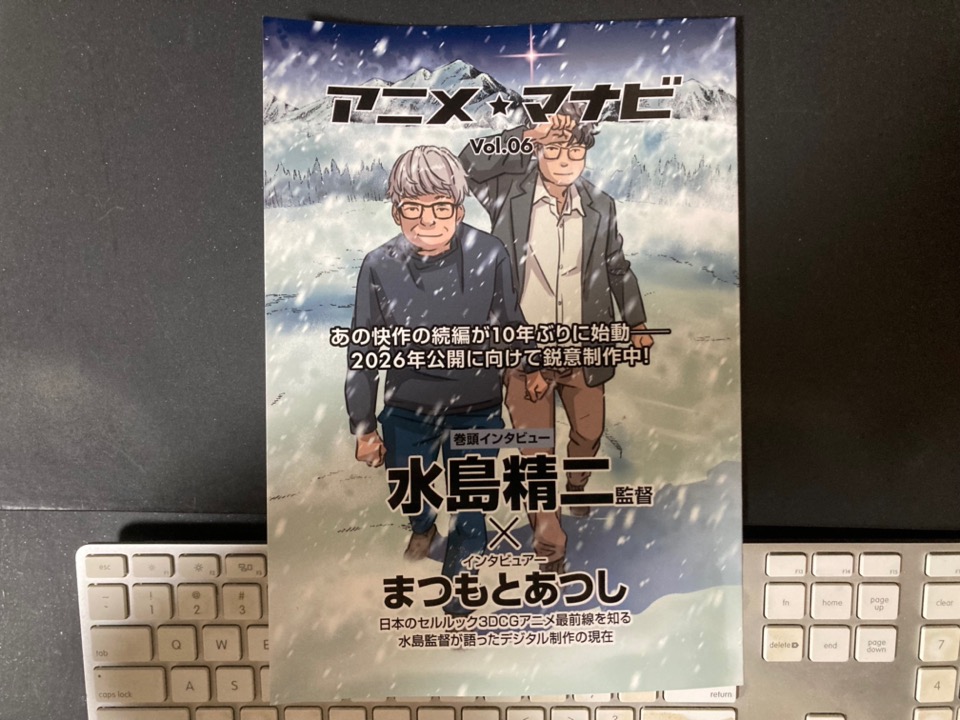 「アニメ・マナビ Vol.06」という冊子の表紙が写っていますね。表紙には、監督の水島精二さんとデジタル制作に詳しいと思われるまつもとあつしさんが登場している様子が描かれています。また、「10年ぶりに始動」「2026年公開に向けて鋭意制作中！」という文言から、注目の続編プロジェクトが紹介されていることがわかります。